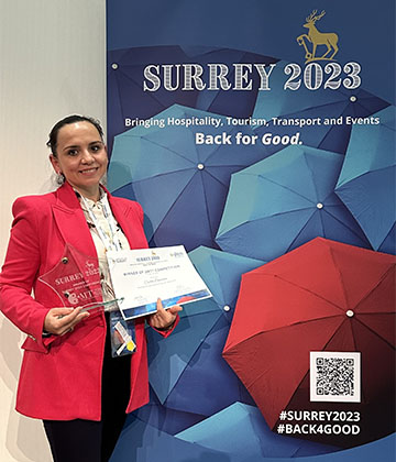  Csilla Demeter holding her award in front of Surrey 2023 Conference screen,