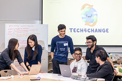 Participants at the 2026 Tech for Change event, in front of a screen with the event logo