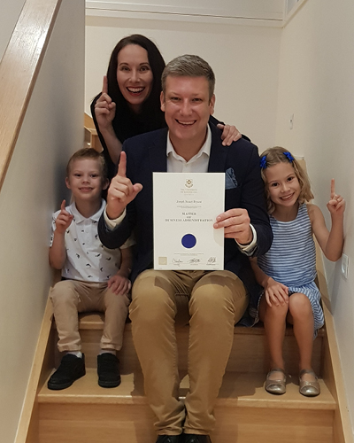 UQ MBA alumnus Joe Bryant with his family, holding his certificate of completion