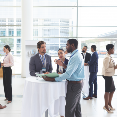 A group of people in corporate attire are networking around a high bar table