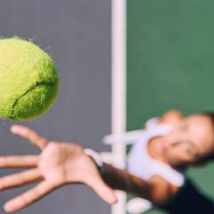 Woman throwing tennis ball up in air