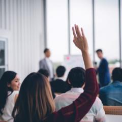 Woman in foreground has arm raised to ask a question