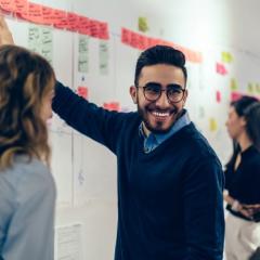 Man in blue sweater pointing at whiteboard with colourful post-it notes
