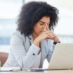 A woman is sitting at her laptop with her face in her hands.
