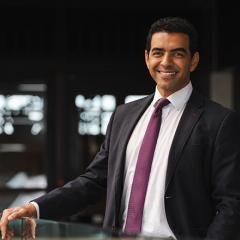 Dr Alex Chaudhuri standing in UQ building with hand on railing 