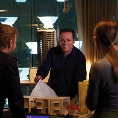 Jan Bodnaruk leading over a table with construction figures talking to two people 
