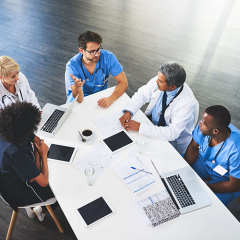 Doctors and nurses discussing business at a board table with laptops and notebooks 
