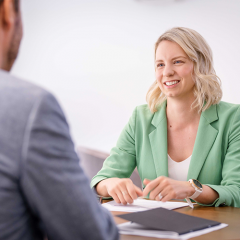 Two mba students sitting at desk talking to each other with notebooks on desk 