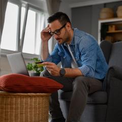 Man with a laptop looking worriedly at a credit card