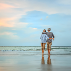 middle age couple holding each other while walking along beach at sunset