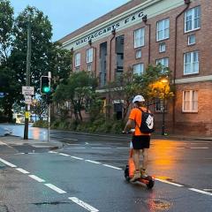 Man in high-vis riding an e-scooter across a road
