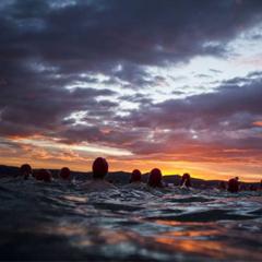 Swimmers in the water with a sunrise in background
